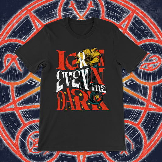 Black unisex t-shirt with the phrase “I Grow Even in the Dark” in stylized red, white, and yellow lettering, adorned with a blooming lily and golden stars. Styled against an arcane, rune-covered background in navy and red.